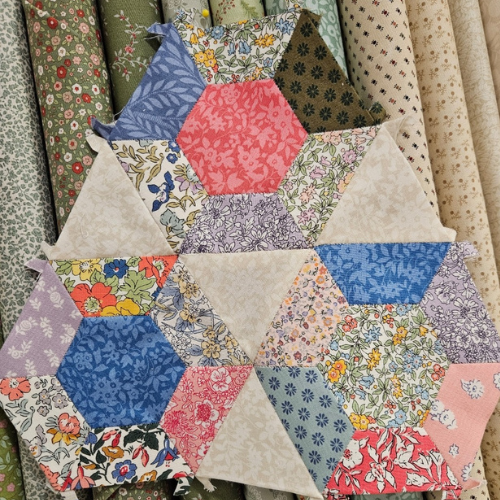Hexagonal patchwork quilt with floral and geometric patterns on a fabric background.