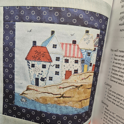 Textile art piece with houses on fabric, placed inside an open book.