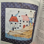 Textile art piece with houses on fabric, placed inside an open book.