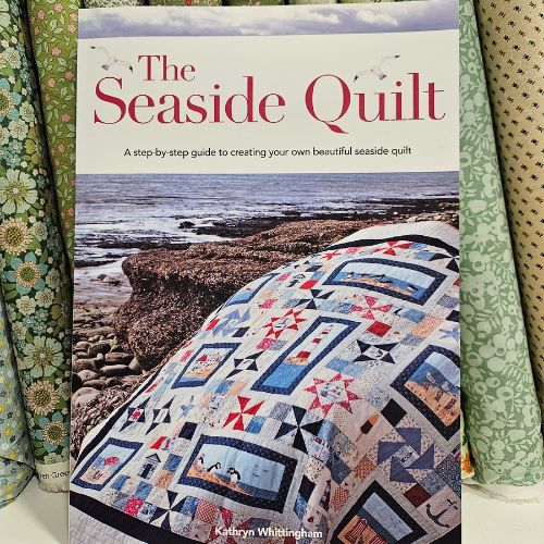 Book titled 'The Seaside Quilt' with a quilt displayed on the cover, featuring a scenic coastal view.