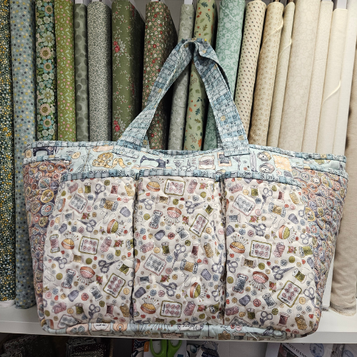 Fabric bag with sewing-themed pattern in front of fabric rolls