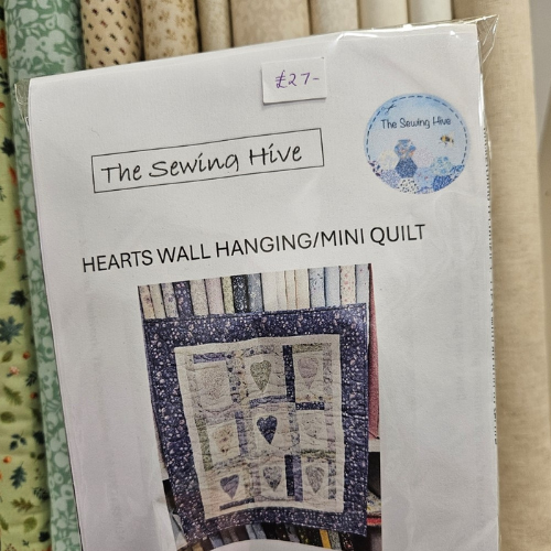 Package of 'Hearts Wall Hanging/Mini Quilt' from The Sewing Hive with fabric swatches in the background.